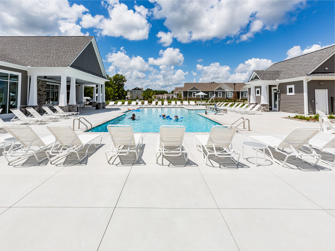 Pool with three people in it. Blue skies and pool chairs.