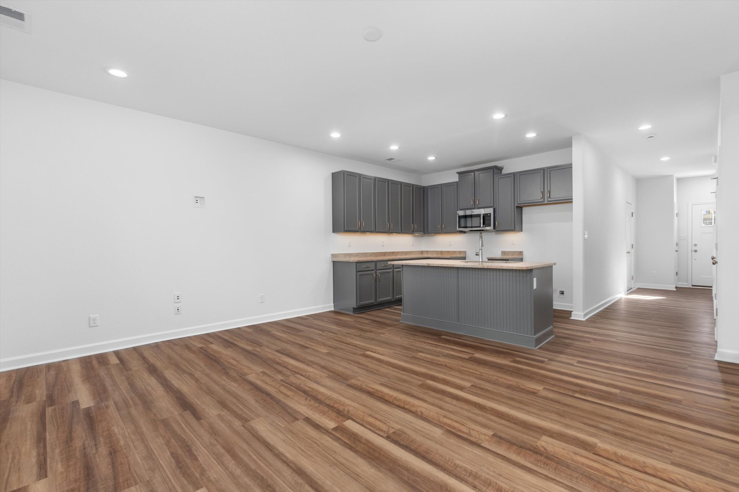 A bright, vacant kitchen with warm wood floors and stylish gray cabinets, offering a contemporary and open feel